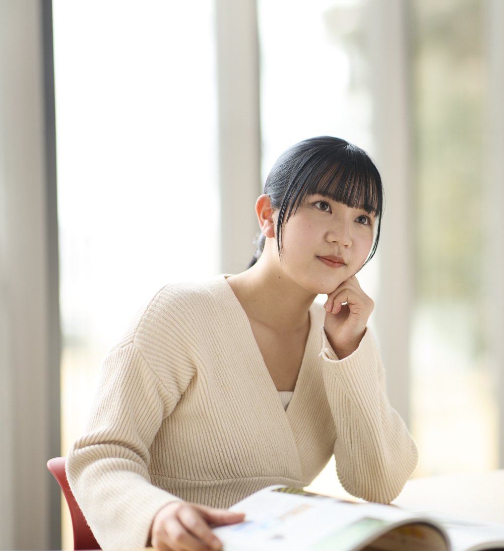 窓辺の席で頬に手を添えて考える学生